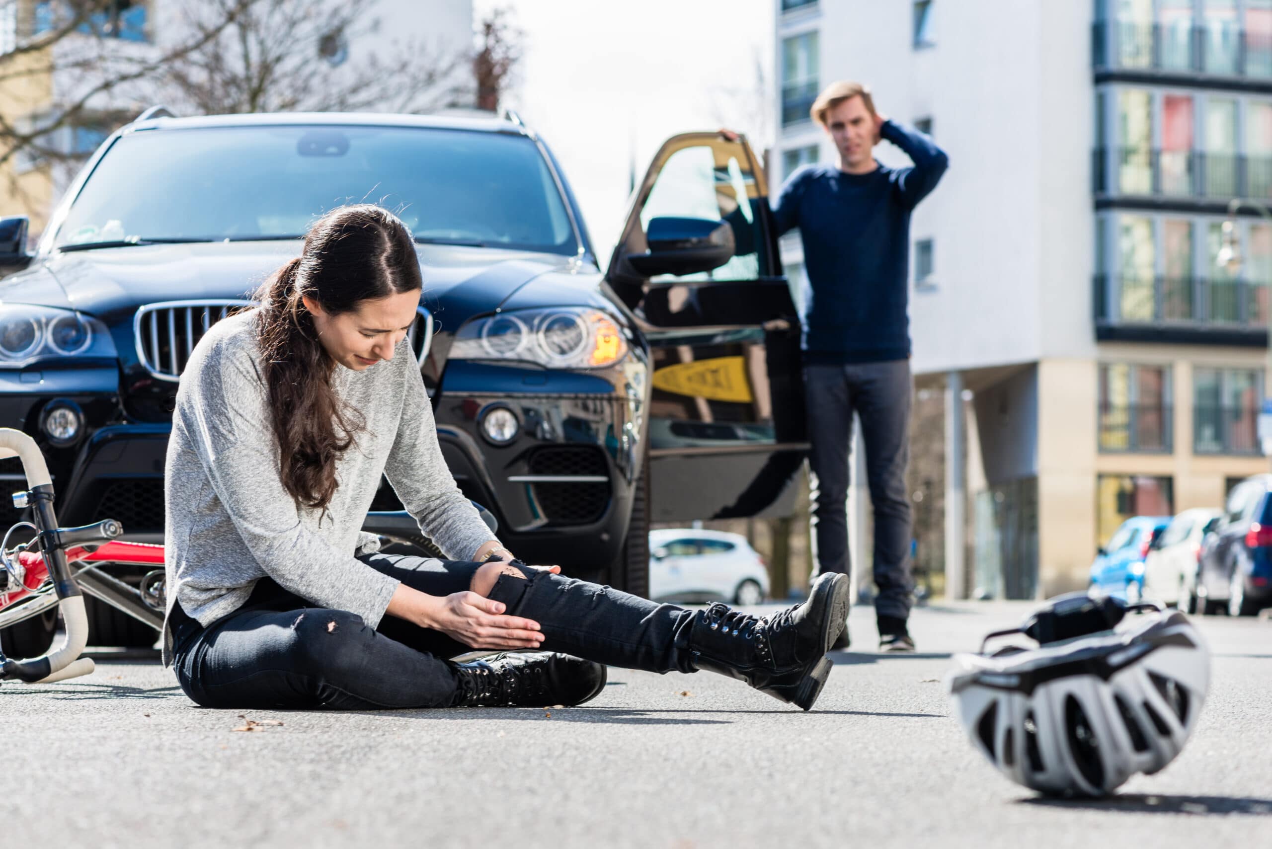 Full length of a young female bicyclist fallen down on street with serious injuries after traffic accident with the 4x4 car of a young man