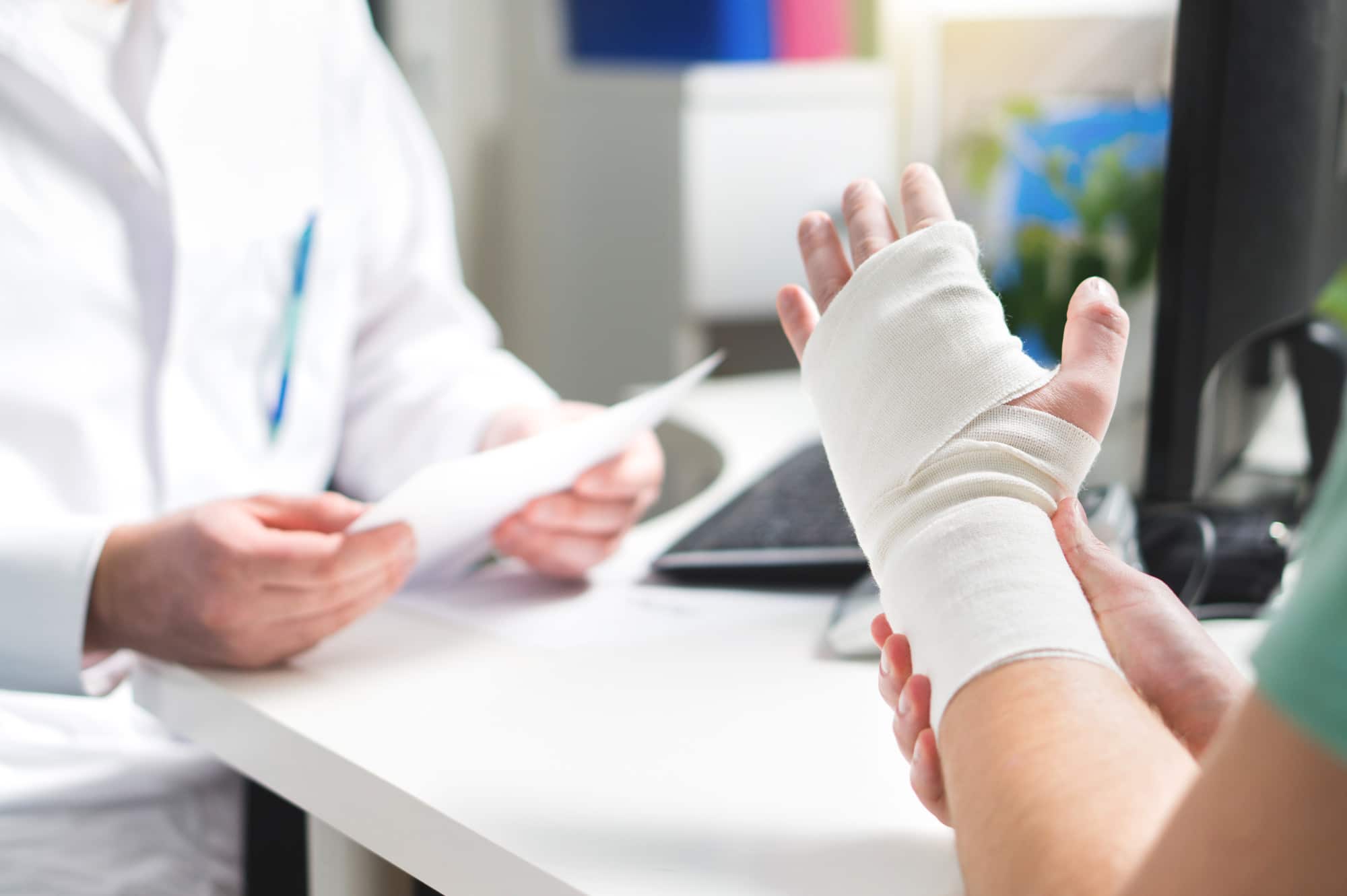 Injured patient showing doctor broken wrist and arm with bandage in hospital office or emergency room. Sprain, stress fracture or repetitive strain injury in hand. Nurse helping customer. First aid.